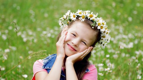 On a chamomile lawn, a sweet girl in a wreath of daisies, smiling, pressing her hands to her cheeks