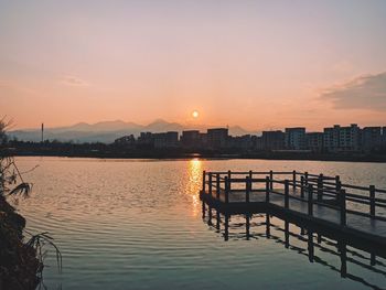 Scenic view of river by buildings against sky during sunset