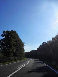 Road amidst trees against clear blue sky