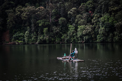 People rowing boat in lake against trees