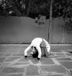 Rear view of woman sitting on footpath against wall