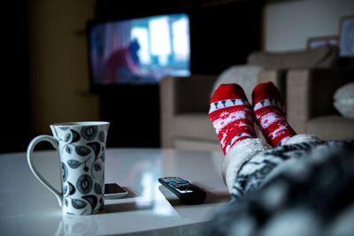 Low section of woman in warm clothing sitting by cup and technology on table at home