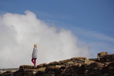 Man standing on rock formation against sky