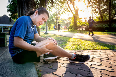 Full length of man sitting on sidewalk in city