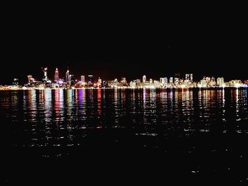 Illuminated cityscape by sea against sky at night