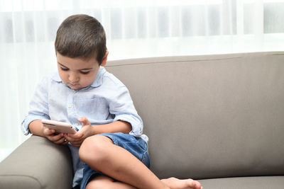 Rear view of boy looking through mobile phone at home