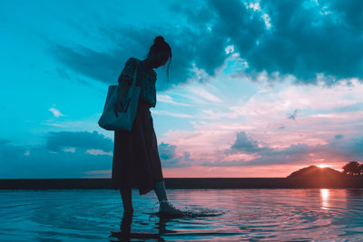 Woman standing by sea against sky during sunset