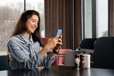 Young woman using phone while sitting in restaurant