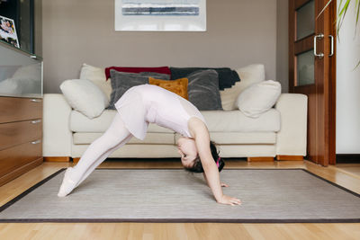 Side view of little girl in leotard doing exercise on floor during dance rehearsal at home