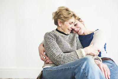 Mother and daughter sitting against white wall