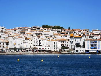 Sailboats in sea by town against clear blue sky