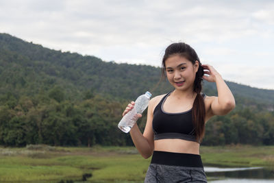 Portrait of smiling woman holding water bottle while standing against mountain