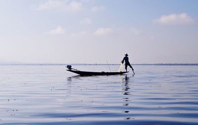 Silhouette fisherman fishing in lake against sky