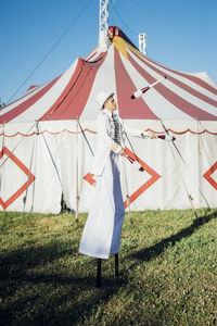 Male artist juggling pins while standing with stilts on meadow