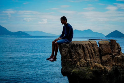 Woman sitting on rock looking at sea against sky