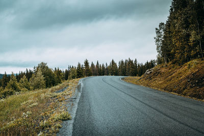 Empty road amidst trees against cloudy sky