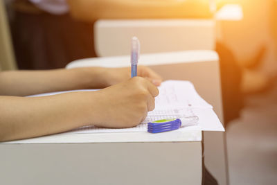 Cropped hands of woman writing on paper while sitting on table