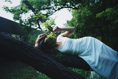 Low section of man sitting by tree against plants