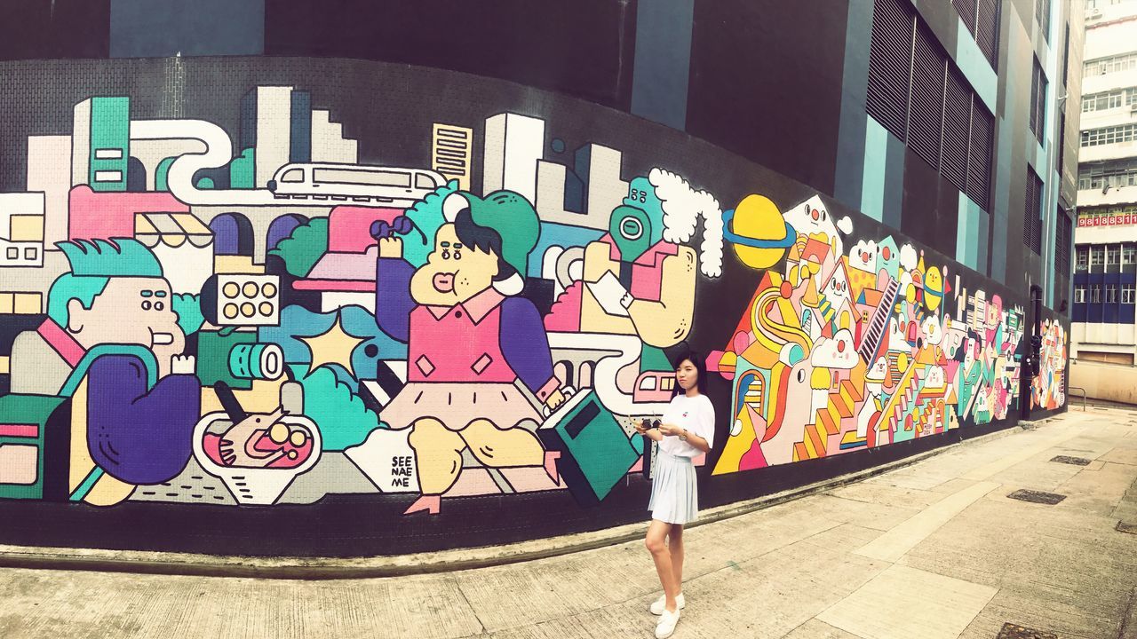 WOMAN STANDING ON MULTI COLORED WALL