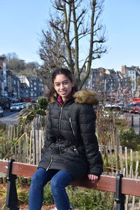 Portrait of smiling girl wearing warm clothing while sitting in city