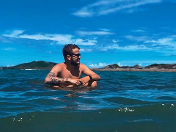 Shirtless man sitting in sea against blue sky