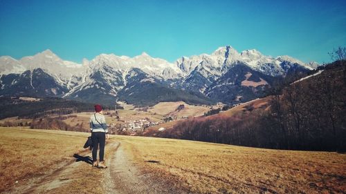 Rear view of woman standing on dirt road against mountains