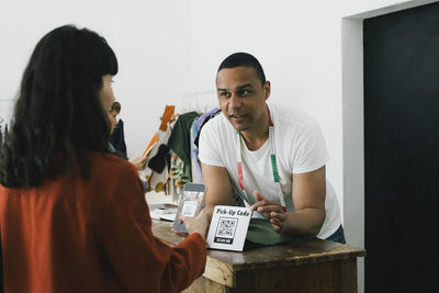 Tailor pointing at bar code scanner while talking to customer in store