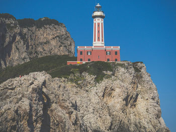 Low angle view of lighthouse by building against clear blue sky