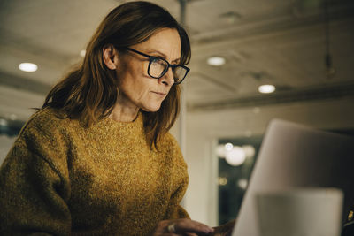 Determined mature female entrepreneur working late while using laptop at workplace