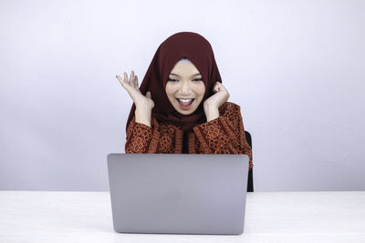 Portrait of smiling young woman using phone against wall