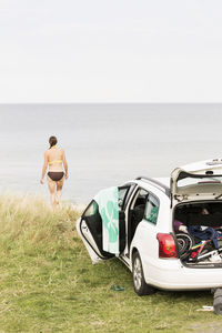 Car at beach against woman walking towards sea