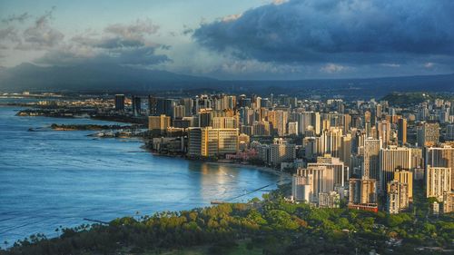 View of city at waterfront against cloudy sky