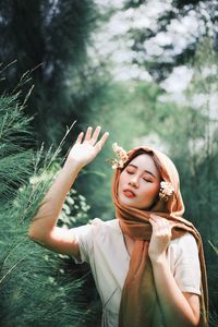 Young woman with eyes closed gesturing against trees