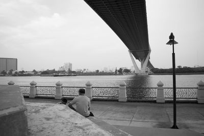 Rear view of man on bridge over river in city against sky