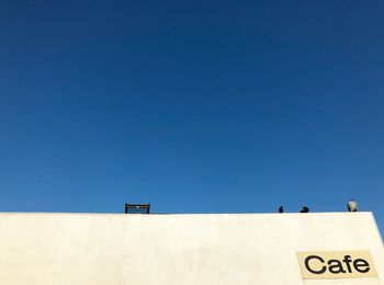 Low angle view of text on building against clear blue sky