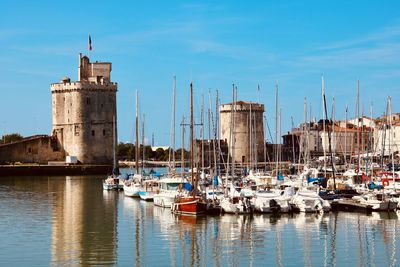 Sailboats moored in harbor against sky in city