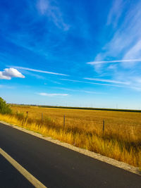 Empty road by grassy landscape against blue sky