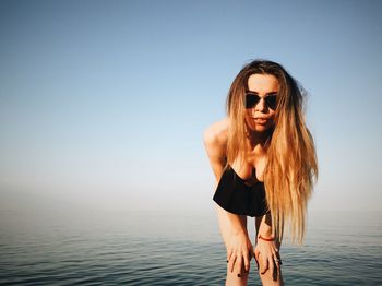 Portrait of beautiful woman wearing sunglasses at beach against clear blue sky