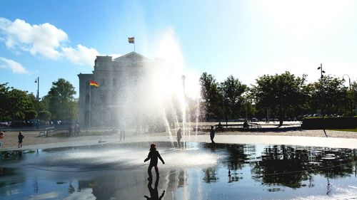 Children playing by fountain in park against sky