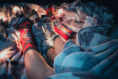Low section of couple wearing socks lying with illuminated string lights on bed at home