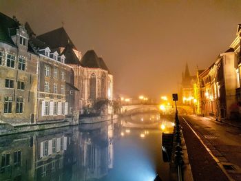 Illuminated buildings by canal against sky in city at night