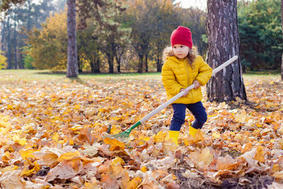 Cute kid standing with broom by trees during autumn