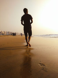 Full length of man on beach against sky during sunset