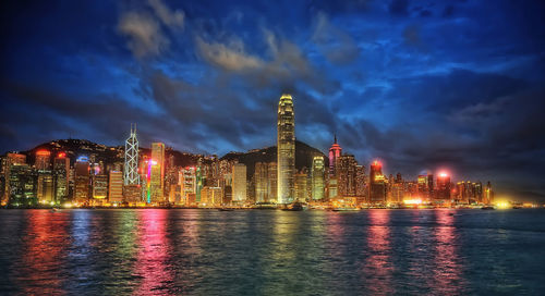 Illuminated buildings by sea against sky at night