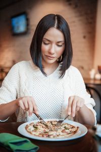 Woman cutting pizza with cutlery in plate at restaurant