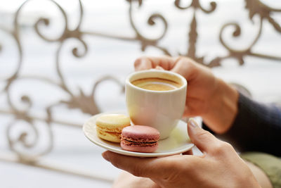 Cropped image of woman holding coffee cup with macaroons in saucer