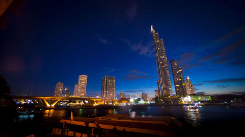 Illuminated buildings by river against sky at night