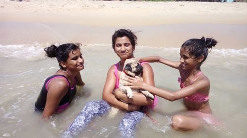Portrait of girl with pug amidst friends bathing at shore