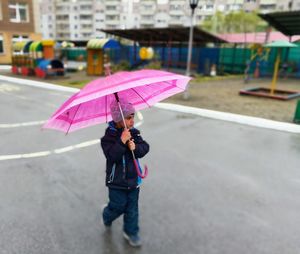 Cute boy holding umbrella while walking on road