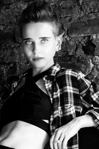 Portrait of young woman standing against brick wall